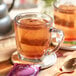 A glass mug of brown Pukka Organic Night Time Berry tea with a tea bag on a saucer.