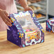 A woman holding a Southern Champion cake box with a Dia de los Muertos design and a clear plastic window over a cake.