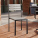 A Lancaster Table & Seating black outdoor chair with gray faux teak slats on a brick patio.