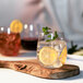 A Carlisle stemless wine glass filled with ice water and lemon slices on a wooden board.