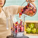 A woman pouring Wyman's Frozen Mango Berry Blend into a blender.