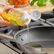 A person pouring LouAna Avocado Oil into a frying pan.