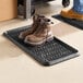 A black rubber boot tray with a diamond pattern, holding a pair of brown work boots.