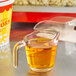 A measuring cup with LouAna Fluffy Pop Popping Oil, a yellow liquid.