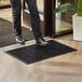 A black 2' x 3' rubber scraper mat with a wave pattern, drainage holes, and beveled edge placed at an entryway.