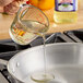 A person pouring LouAna Safflower Oil from a measuring cup into a pan on a stove.