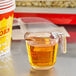 A measuring cup with LouAna Premium Buttery Topping Oil in it next to a cup of popcorn.