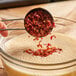 A measuring cup pouring dried red bell pepper into a glass bowl.