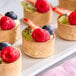 A group of White Toque quiche and tart shells filled with fruit on a white plate.