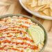 A bowl of tortilla chips with Valentina Black Label Mexican hot sauce and lime slices.