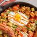 A skillet of food with a fried egg, sausage, and potatoes.