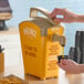 A person using a Heinz yellow plastic countertop pump to dispense mustard.