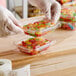 A gloved hand holds a Inline Plastics rectangular clear plastic container full of candy.