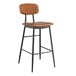 A Lancaster Table & Seating black barstool with brown vinyl cushion on a table in a bar.