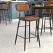 A Lancaster Table & Seating Mid-Century Black Barstool with Cognac Vinyl Padded Seat and Backrest.