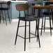 A Lancaster Table & Seating black bar stool with espresso wood backrest and black vinyl seat.