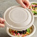 A person holding a World Centric compostable fiber lid over a bowl of food.