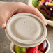 A hand holding a World Centric compostable fiber bowl with a lid filled with fruit.