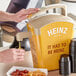 A person pouring mustard into a container using a Heinz Honey Mustard pump.