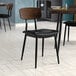 A Lancaster Table & Seating black chair with black vinyl padded seat and espresso wood backrest on a table in a restaurant dining area.
