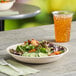 A World Centric compostable fiber bowl filled with salad on a table with a glass of iced tea.