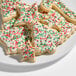 A plate of Christmas-themed sugar cookies decorated with white icing and red and green nonpareil sprinkles.