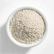 A white bowl filled with small white nonpareil sprinkles.