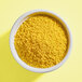 A white bowl filled with small yellow nonpareil sprinkles.
