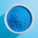 A white bowl filled with small, round, bright blue nonpareil sprinkles.