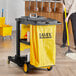 A woman using a yellow mop to clean a floor with a Lavex janitorial cart.