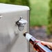 A hand using a bottle opener to open a Choice stainless steel beverage bottle on an outdoor patio.