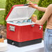 A woman opening a red Choice Steel Beverage Cooler filled with drinks on a counter.
