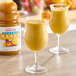 Two glasses of yellow Dr. Smoothie Classic Mango smoothie on a table.
