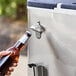 A hand using a bottle opener on a stainless steel beverage cart to open a bottle of beer.