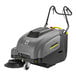 A grey and yellow Karcher walk-behind sweeper with a brush and battery.