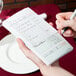 A person writing on a green and white Choice guest receipt on a table.