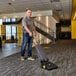 A man using a Karcher Ranger upright vacuum cleaner to clean a carpet in a corporate office.