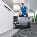 A woman using a Karcher cordless carpet sweeper to clean the carpet in an office.