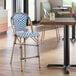 A counter height outdoor side stool with a navy and white chevron weave design and rattan frame.