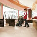 A woman using a Karcher walk-behind cylindrical floor scrubber to clean a restaurant floor.