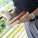 A person holding a footlong hot dog and french fries in a white paper food tray.