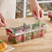 A hand using a plastic clamshell container to hold cut strawberries.