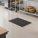 A black rubber anti-fatigue floor mat with a diamond pattern, measuring 2 feet by 3 feet and 3/4 inch thick, placed in a commercial kitchen setting.