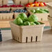 A close up of a cardboard Choice Produce Basket filled with brussels sprouts on a table.