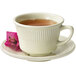 A white saucer with a cup of tea with a pink flower on it.