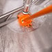 An orange Vikan tank brush head with stiff bristles in foamy water.