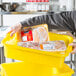 A man holding a Vollrath yellow perforated drain box full of food.