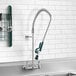 A Krowne wall-mount pre-rinse faucet above a sink with utensils.