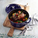 A Staub dark blue enameled cast iron Dutch oven filled with meat and vegetables.