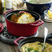 A red Staub enameled cast iron pot with a lid on a table with food inside.